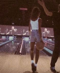 two people standing in front of a bowling alley with bowling balls on the floor and one person holding a basketball