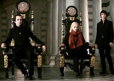 three people sitting on thrones in front of columns