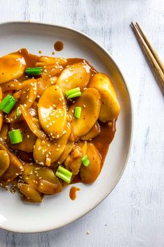 a white plate topped with meat covered in gravy and green onions next to chopsticks