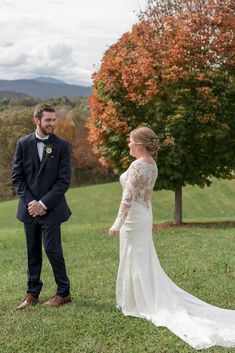 a bride and groom standing in the grass looking at each other with trees in the background