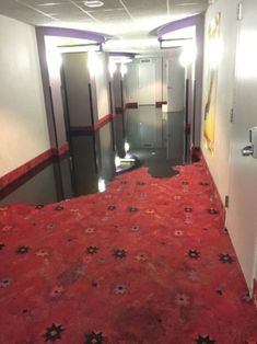 an empty hallway with red carpet and white doors leading to another room that has elevators