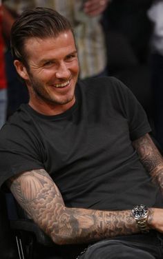 a man sitting in a chair with tattoos on his arms and chest, smiling at the camera