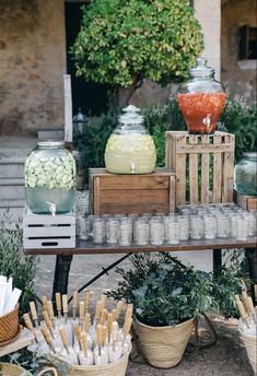 an assortment of jars and candles on a table with plants in baskets next to them