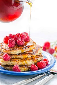 pancakes with raspberries and syrup being drizzled over them on a blue plate