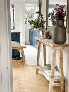 a wooden table sitting in the middle of a room next to a mirror and potted plant