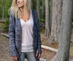 a woman standing in the woods wearing a cardigan