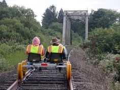 two people in safety vests riding on train tracks