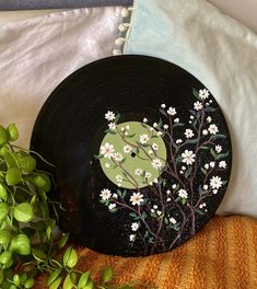 a black plate with white flowers on it sitting next to a green plant and pillow