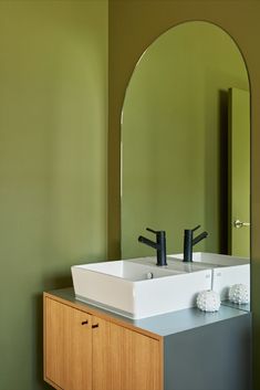 a bathroom sink sitting under a mirror next to a wooden cabinet with two black faucets