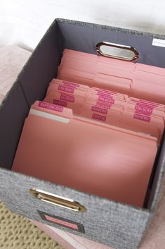 a gray box with pink file folders in it on a beige table cloth covered surface