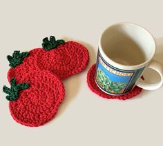 two crocheted strawberry coasters next to a coffee cup on a white table