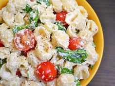 a yellow bowl filled with pasta salad and topped with tomatoes, green beans, and spinach