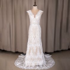 a white wedding dress on display in front of a gray curtained background with a mannequin