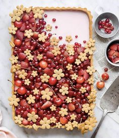 a cake decorated with cherries and flowers on top of a white table next to bowls of strawberries