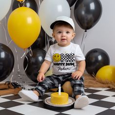 a baby boy sitting in front of balloons with a birthday cake