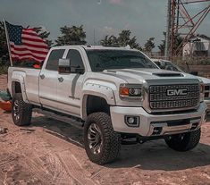 a white truck parked on top of a sandy beach next to an american flag in the background