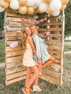 two young women posing for a photo in front of a wooden structure with balloons and flowers