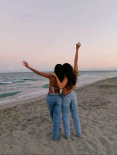 two women are standing on the beach with their arms in the air and one is holding her back