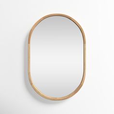 an oval mirror hanging on the wall next to a white wall with a wooden frame