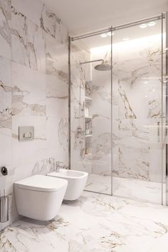 a bathroom with marble walls and flooring, two toilets in the corner next to each other