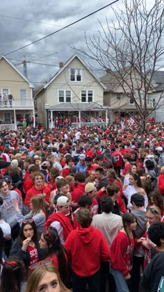 a large group of people standing in the middle of a street with houses behind them