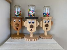 three wooden monkey jars with candy in them on top of a white shelf next to a wall