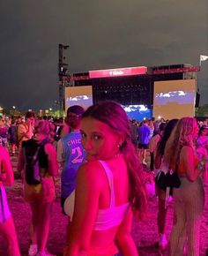 a woman standing in front of a crowd at a music festival with bright lights on the stage