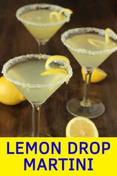 three martinis with lemon garnish sit on a wooden table next to sliced lemons