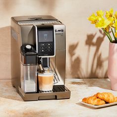 a coffee maker next to some croissants on a table with yellow flowers