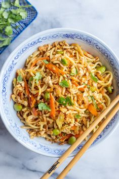 a bowl filled with noodles, carrots and green onions next to chopsticks