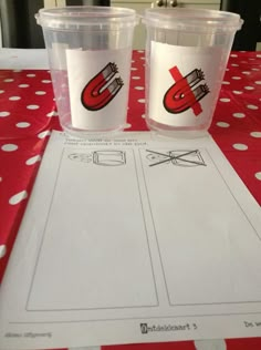 two plastic cups sitting on top of a table next to a piece of paper with the letters