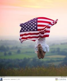 a person holding an american flag on top of a hill with the sun setting in the background