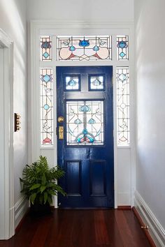 a blue front door with stained glass on the windows and wood flooring, along with a potted plant