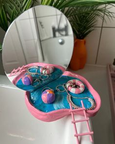 a pink and blue bathtub with jewelry on it in front of a round mirror