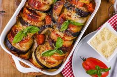 a casserole dish filled with eggplant, tomatoes and other vegetables on a wooden table