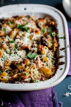 a casserole dish filled with pasta and cheese on a purple cloth next to silverware