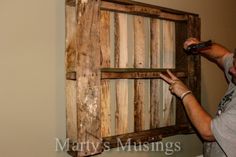 a man holding a remote in front of a wooden frame with strips of wood on it