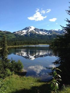 a lake surrounded by trees and mountains with snow on the mountain top in the distance