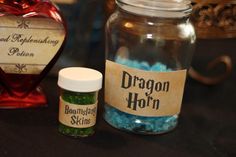 two jars filled with blue and green beads next to a red heart shaped jar on a table