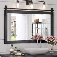 a bathroom sink sitting under a large mirror next to a vase with flowers on it