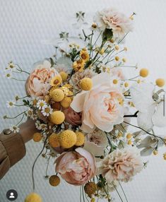 a bouquet of flowers is being held by someone's hand in front of a white wall