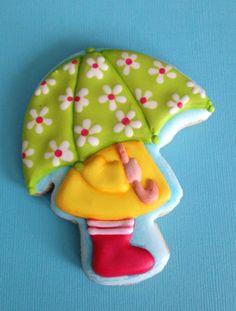 a decorated cookie with an umbrella and boots on it's head, sitting on a blue surface