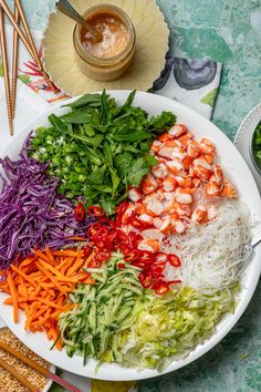 a white plate topped with lots of veggies next to chopsticks and dipping sauce