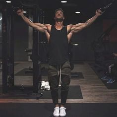 a man standing in front of a gym machine with his arms stretched out and looking up