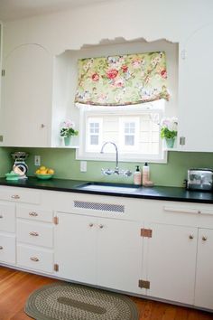 a kitchen with white cabinets and black counter tops next to a green curtained window