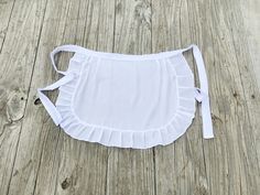 a white top with ruffles on it sitting on a wooden floor next to a pair of scissors