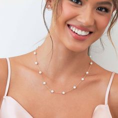 a woman wearing a necklace with white pearls on it and smiling at the camera,