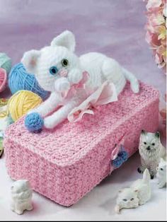 a white cat laying on top of a pink box next to small kitten figurines