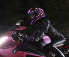 a person riding on the back of a pink motorcycle at night with its lights on