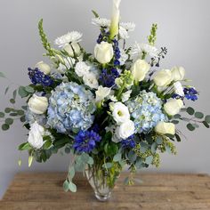 a vase filled with blue and white flowers on top of a wooden table next to a wall